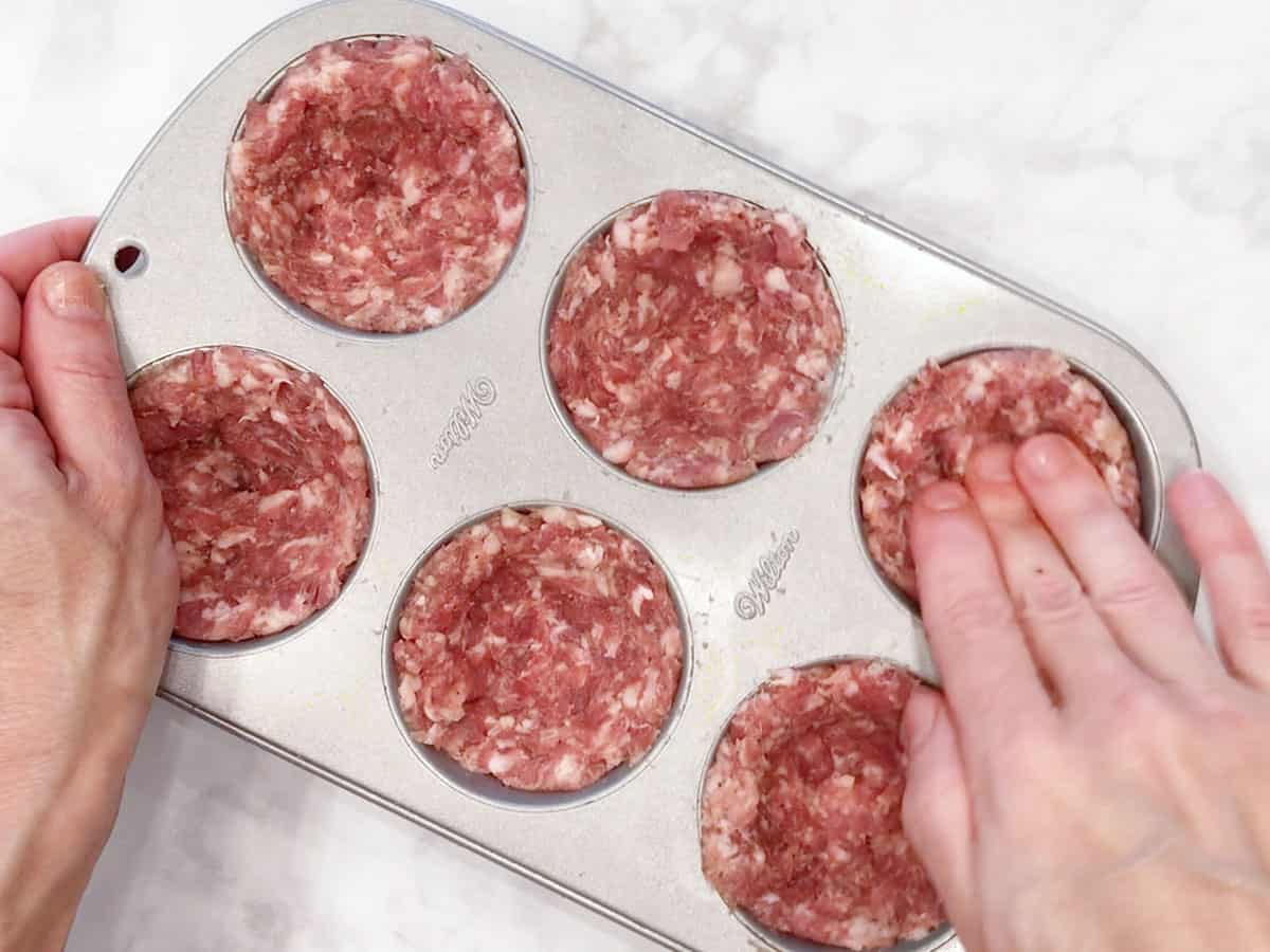 Lining the muffin cups with ground beef.