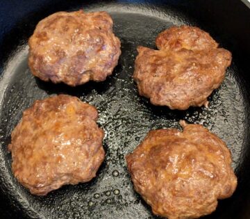 Slightly puffed burgers in a skillet.