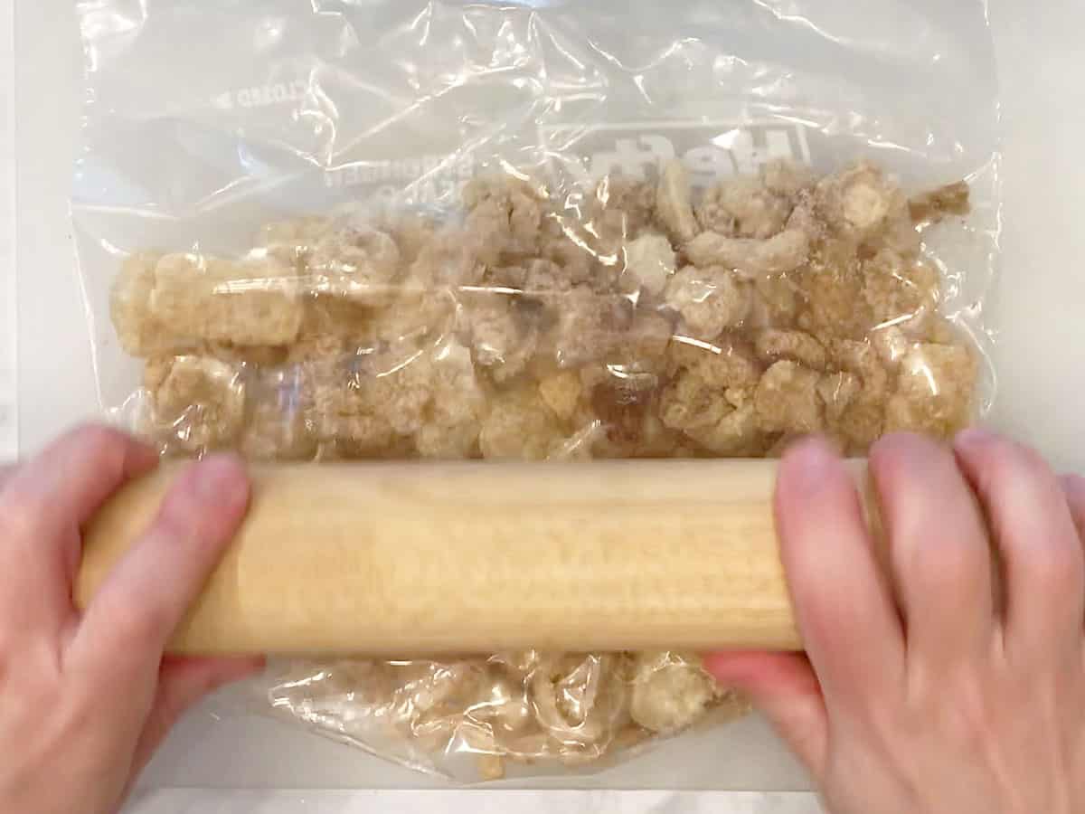 Crushing the pork rinds with a rolling pin.
