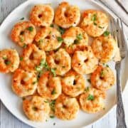 Shrimp parmesan are served on a white plate with a fork.