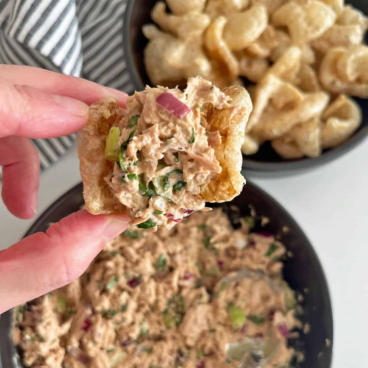 A pork rind is used to scoop tuna salad.