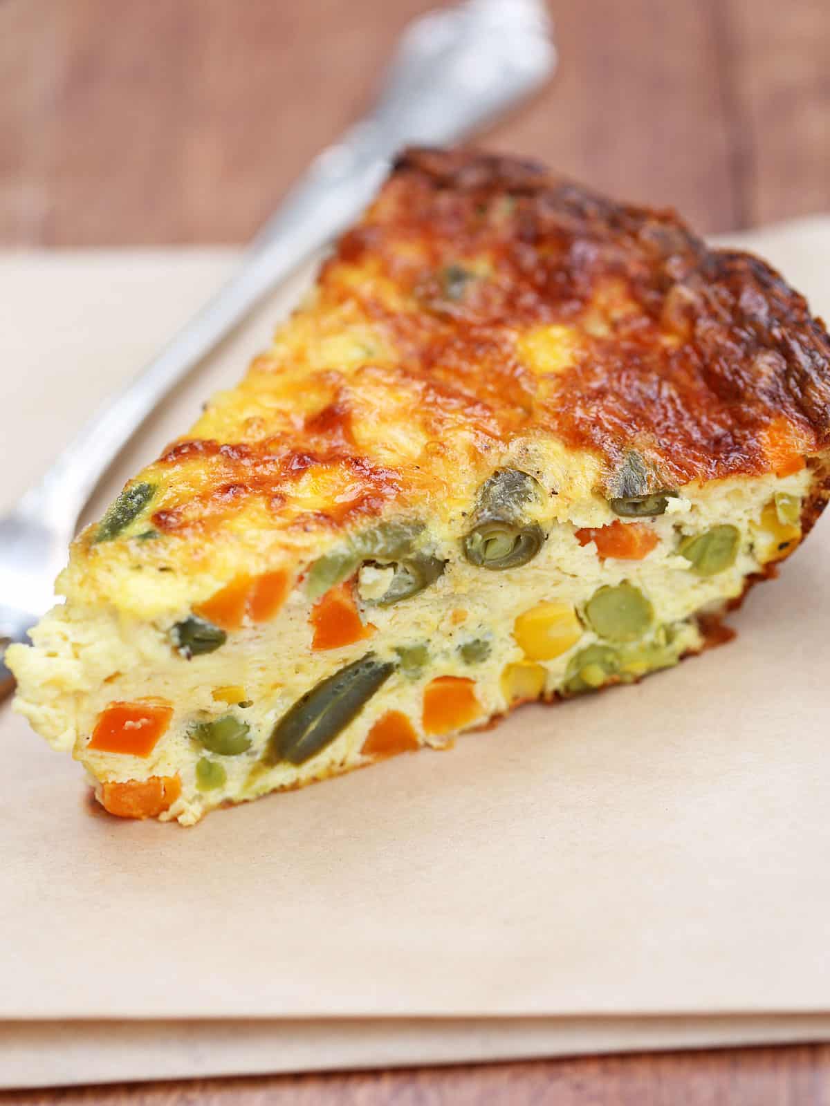 A slice of crustless vegetable quiche is served with a fork.