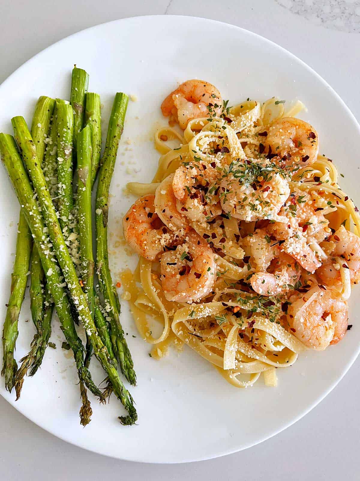 Garlic butter shrimp are served over pasta with a side of asparagus.