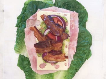 Avocado, tomato, onion, and bacon were added to the sandwich.