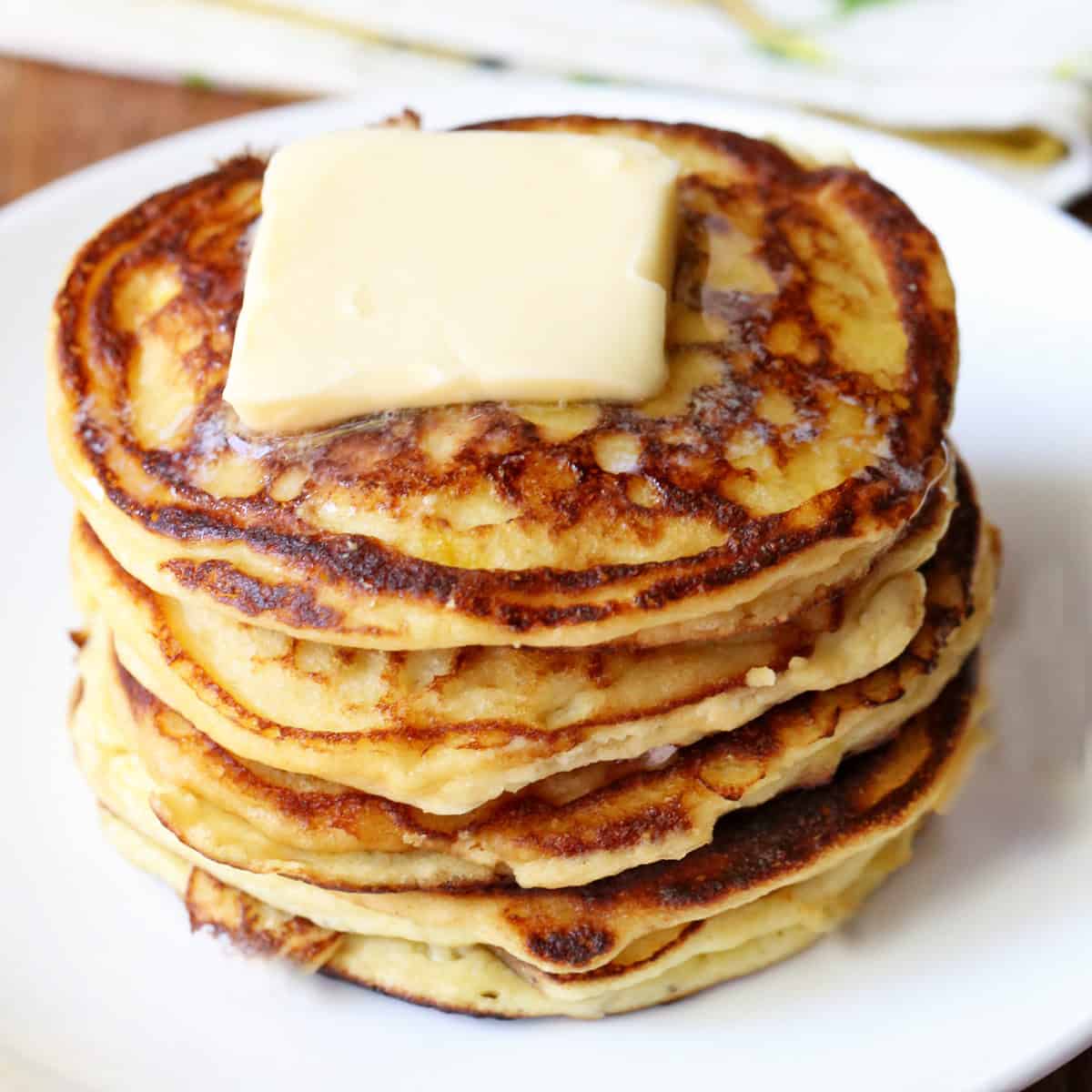 Keto ricotta pancakes are stacked on a white plate and topped with butter.