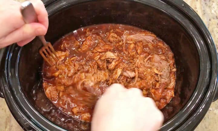 Shredding the pork in the slow cooker pan.