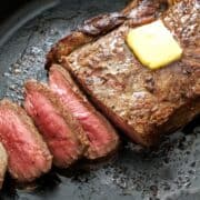 Sirloin steak is served in a skillet, topped with butter.