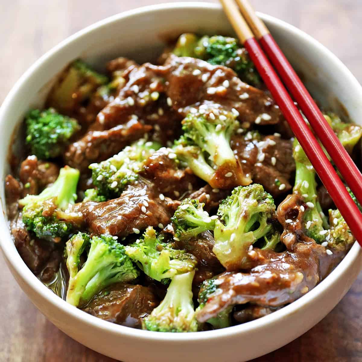 Beef and broccoli is served in a white bowl with chopsticks.