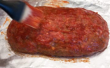 Coating the meatloaf with ketchup.