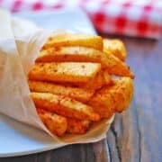 Jicama fries are served on a white plate wrapped in parchment paper.