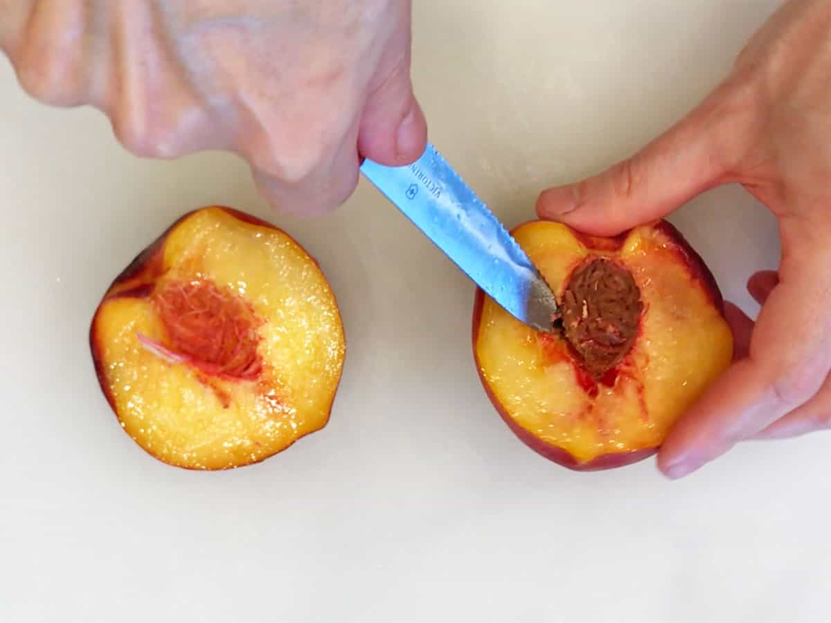 Using a paring knife to loosen the peach pit.