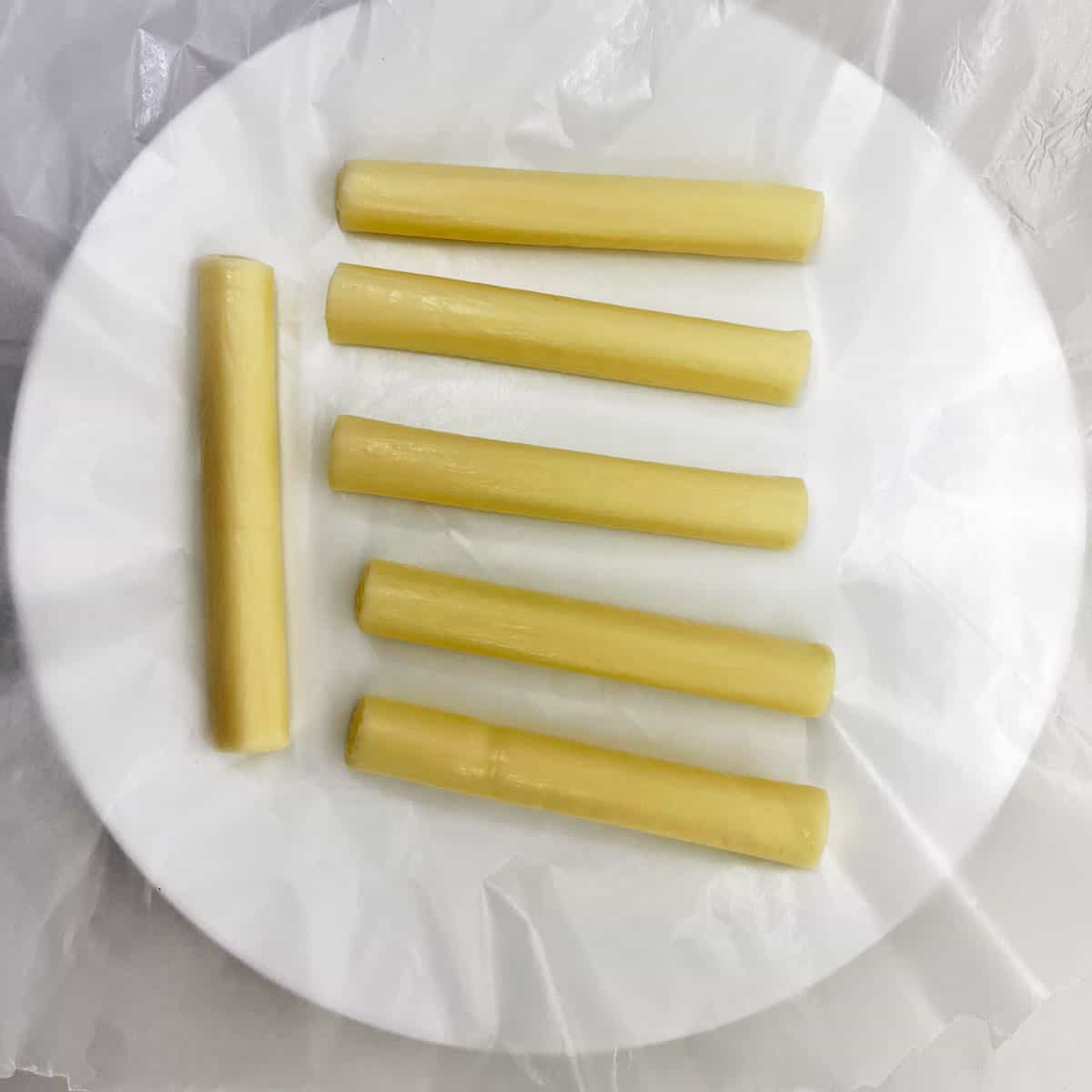 Six mozzarella sticks on a wax paper-lined plate.