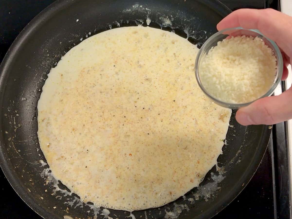 Adding grated parmesan to the cream sauce.
