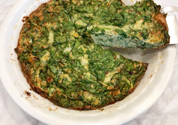 Lifting a slice of spinach frittata from the pan.