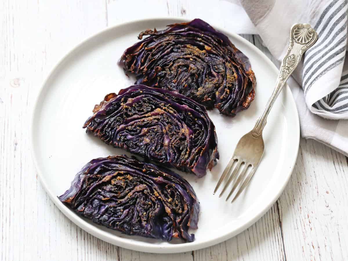 Three slices of roasted red cabbage are served on a white plate with a fork.