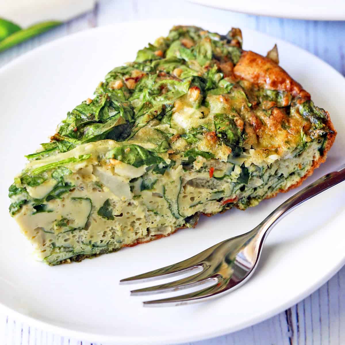 A slice of spinach frittata is served on a white plate with a fork.