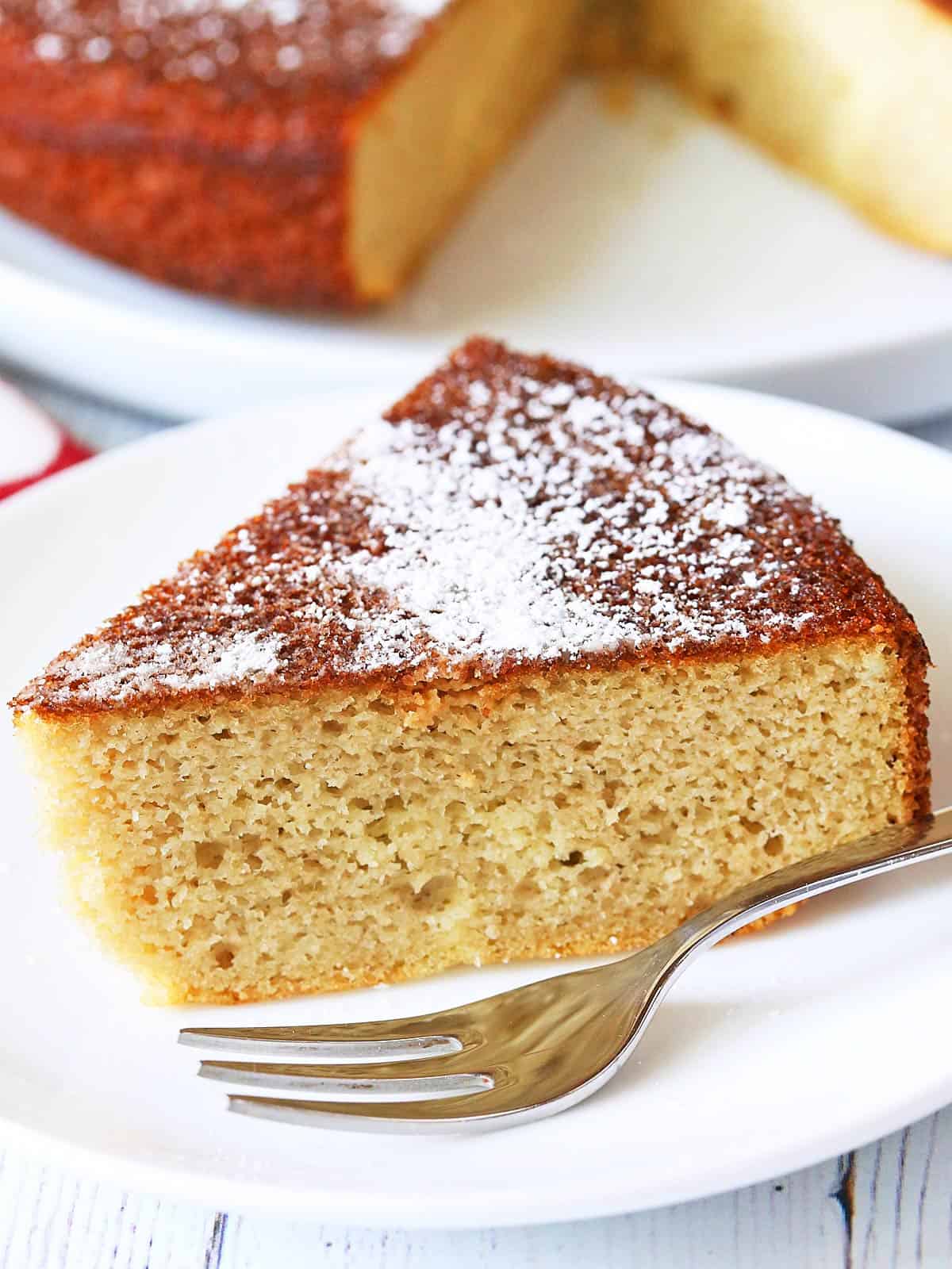 A slice of almond flour cake is dusted with a powdered sweetener.