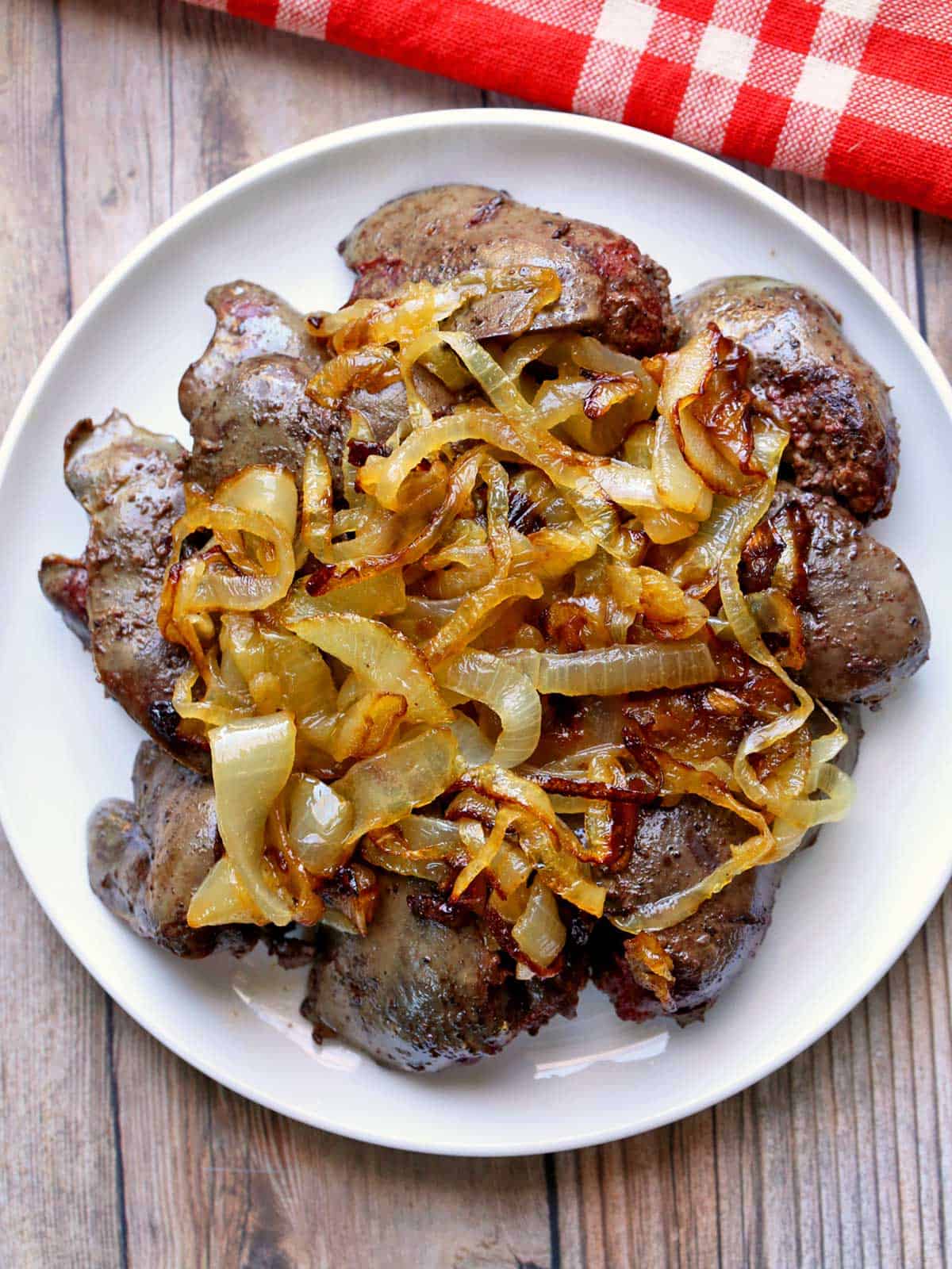 Sautéed chicken livers are topped with onions and served on a white plate with a red napkin.