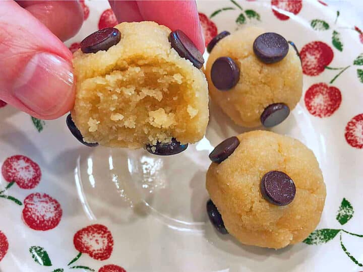 A hand holds a bitten ball of cookie dough.