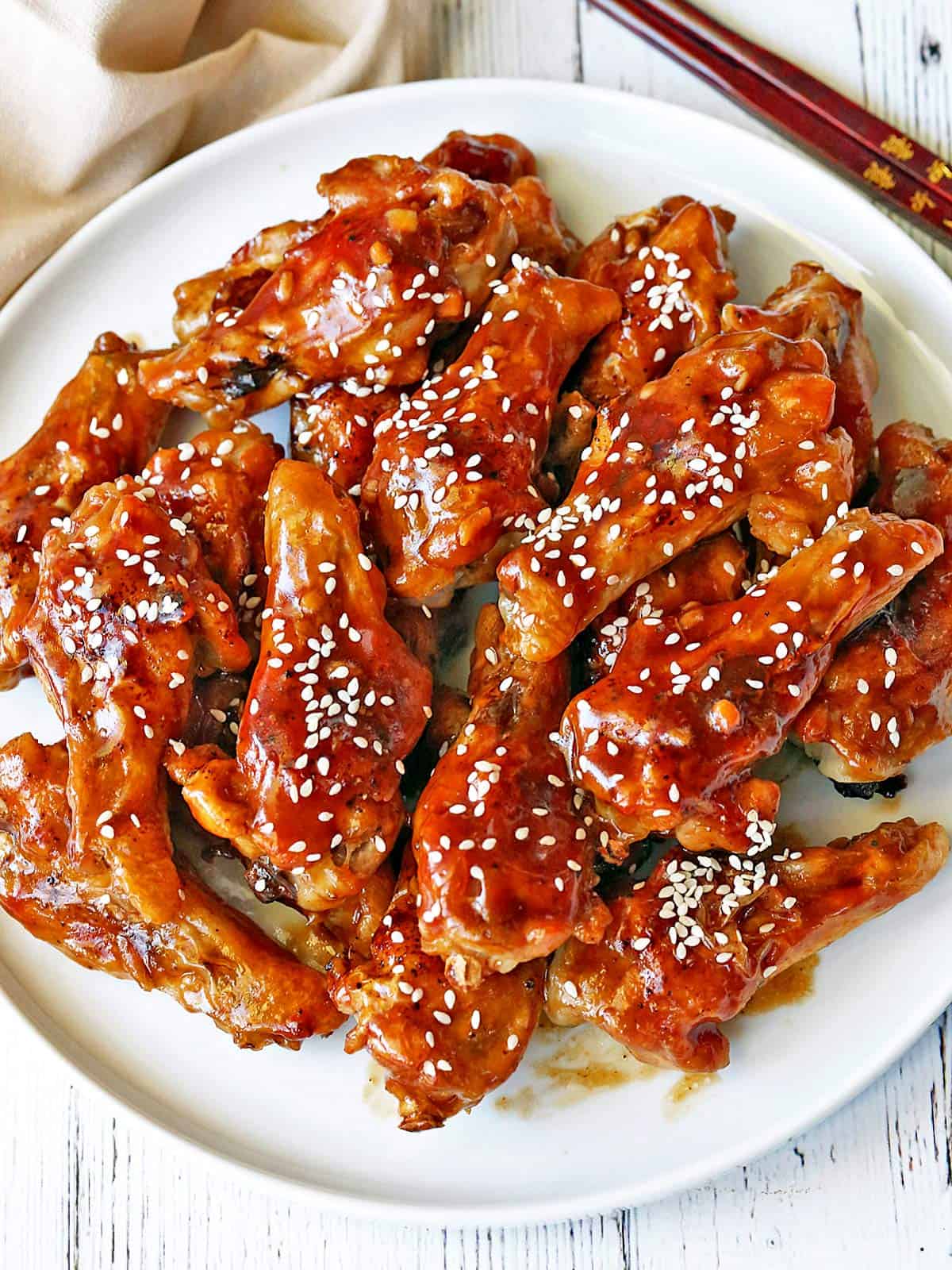 Teriyaki wings are served on a white plate with a napkin and chopsticks.