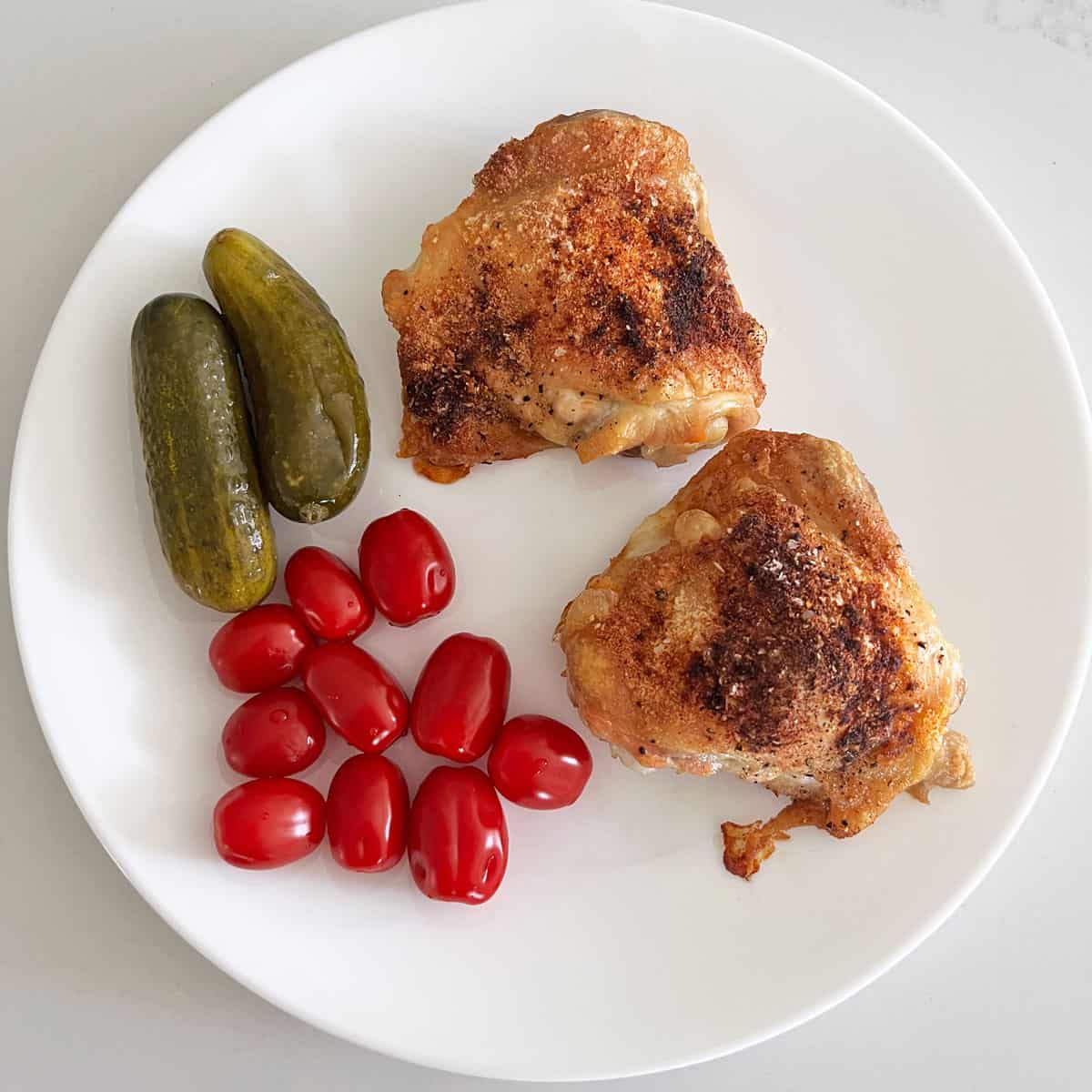 Crispy chicken thighs are served with cherry tomatoes and dill pickles.