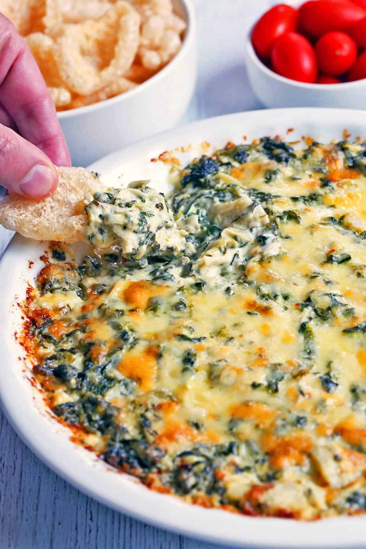 Spinach artichoke dip is scooped with pork rinds.