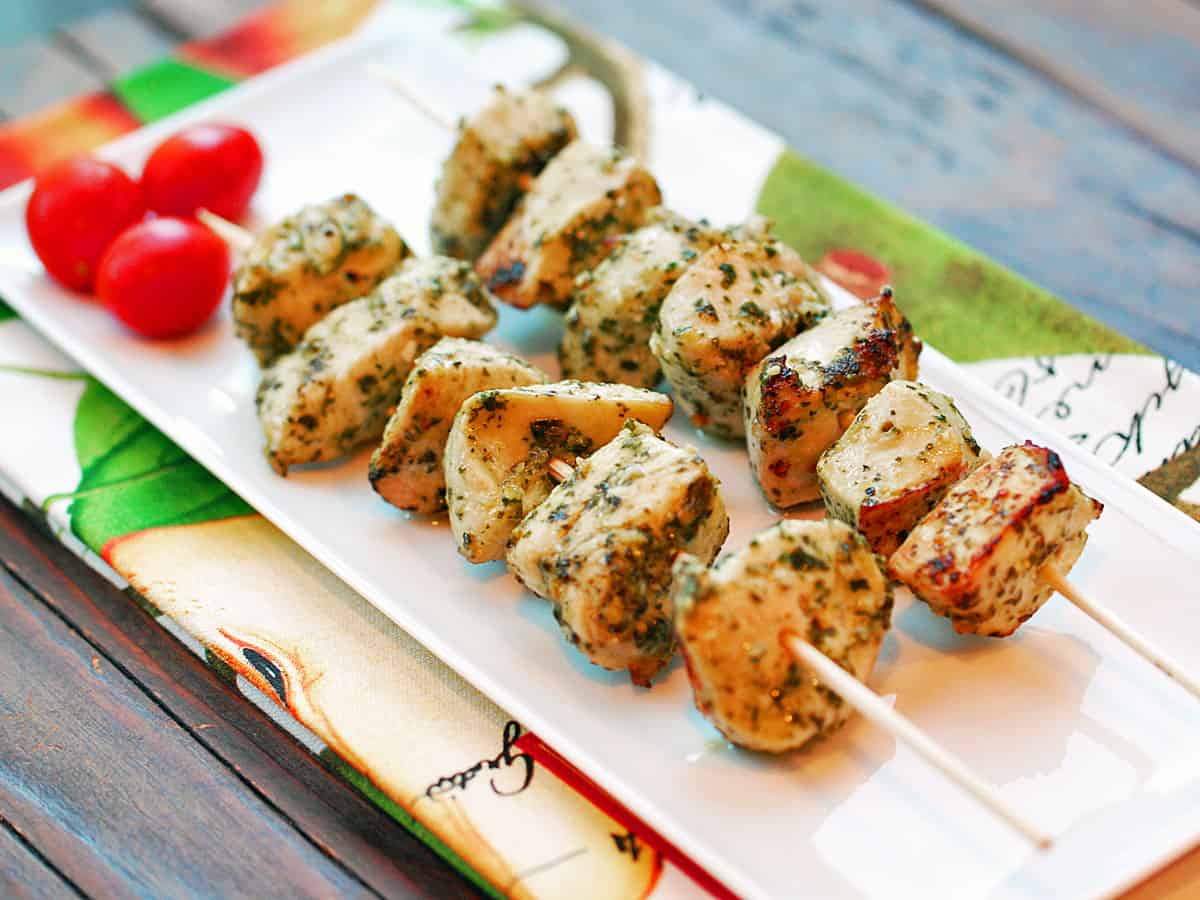 Pesto chicken kabobs are served on a white tray.
