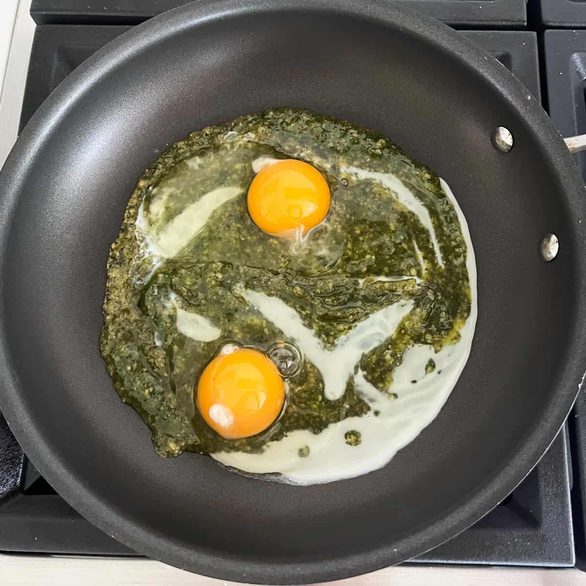 Adding eggs to the pesto in the skillet.