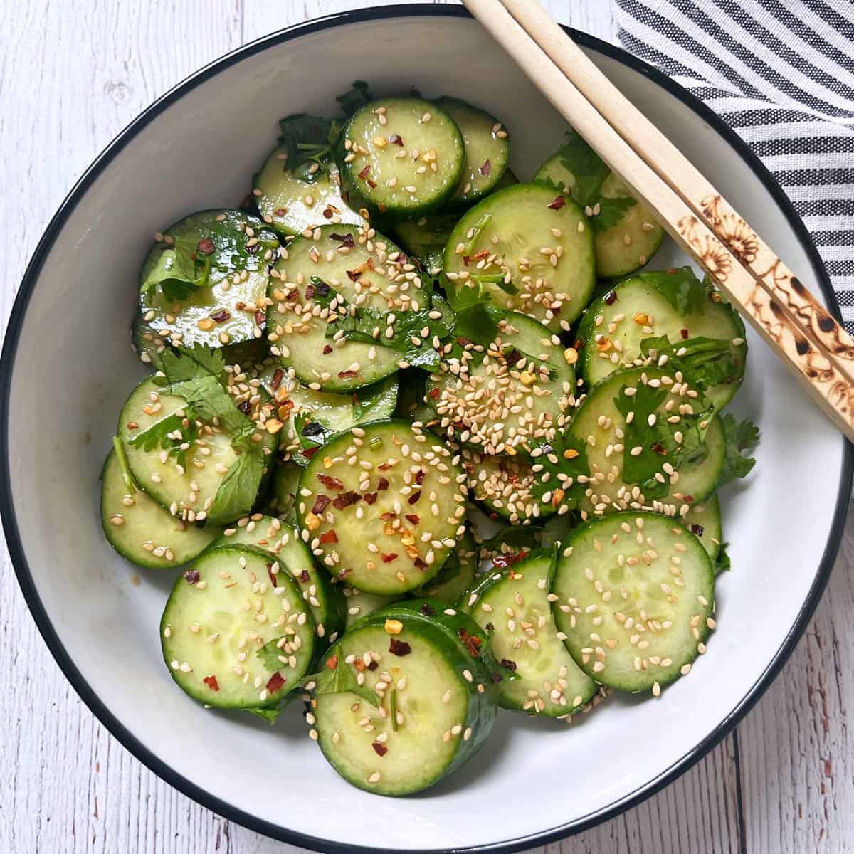Asian cucumber salad is served in a white bowl with chopsticks.