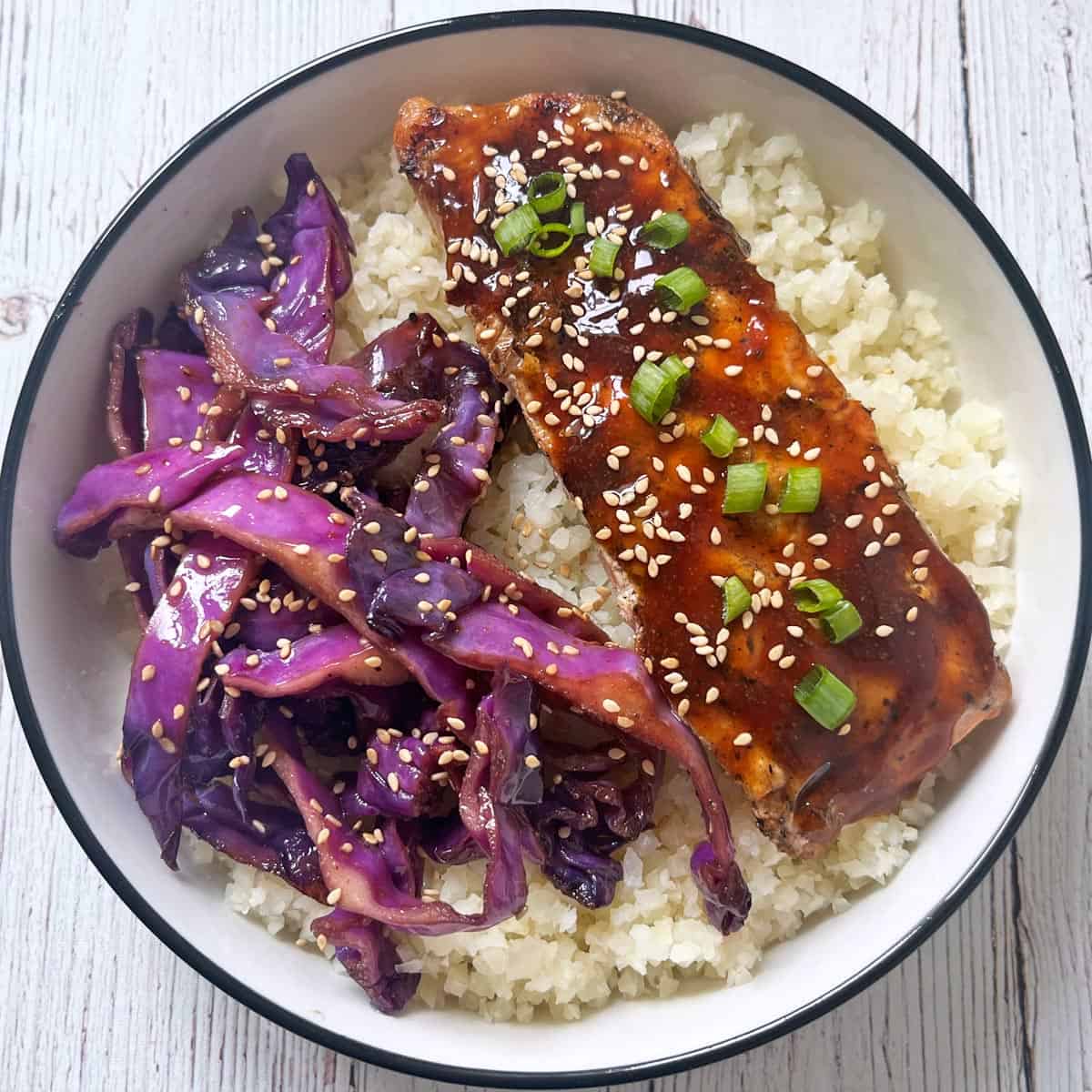 Cabbage stir-fry is served with teriyaki salmon on top of cauliflower rice.