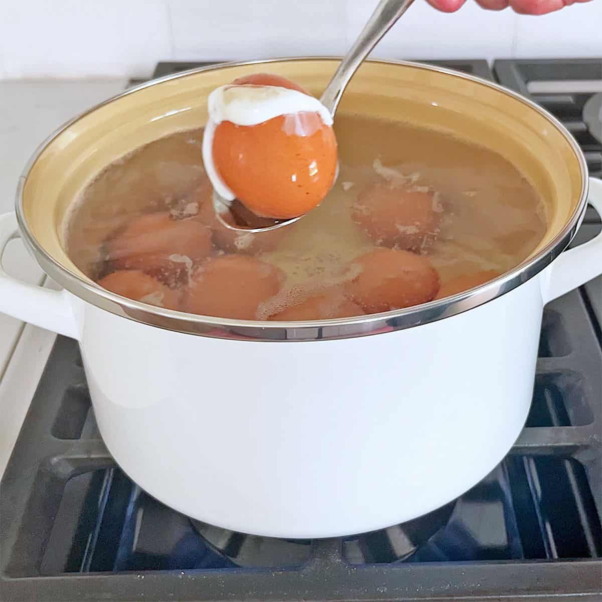 An egg that cracked when lowered into the boiling water is lifted with a spoon.