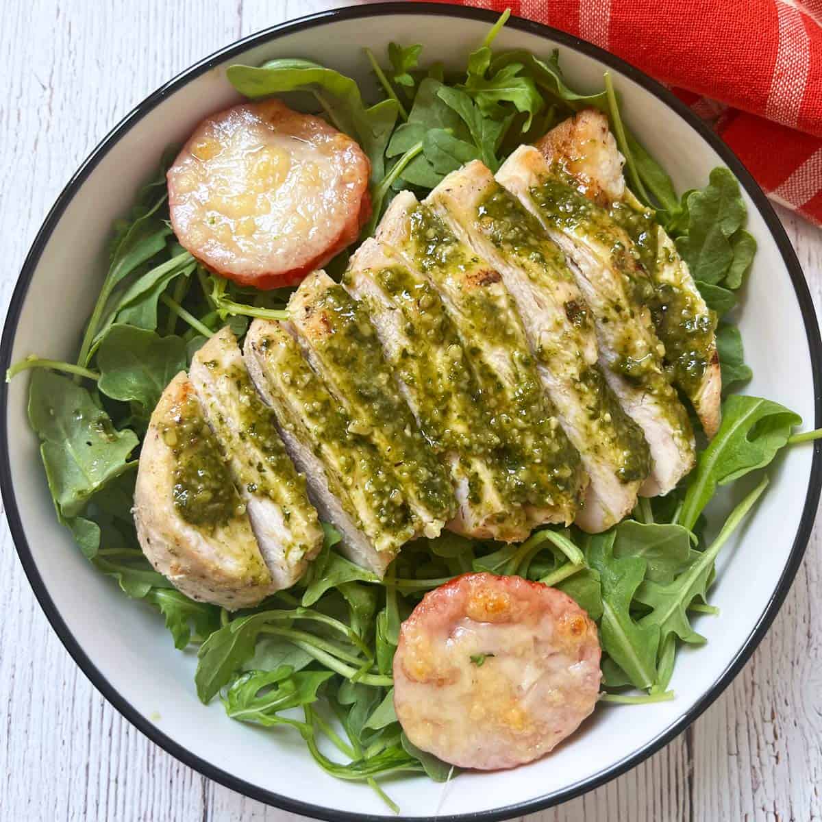 Pesto chicken leftovers are served on a bed of arugula.