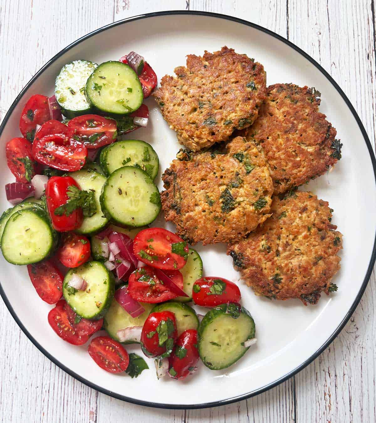 Tuna patties are served with cucumber tomato salad.