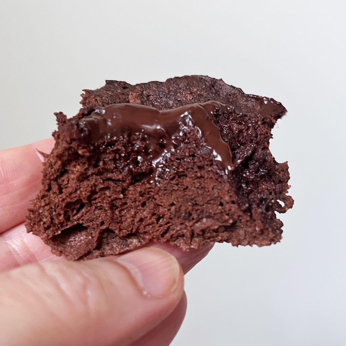 A hand holds a piece of a chocolate mug cake.