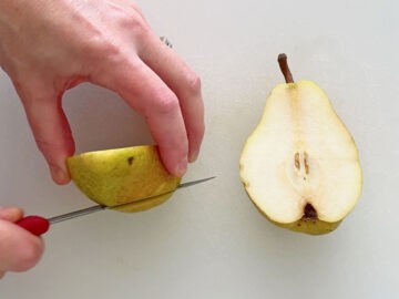 Shaving a thin slice off the peel side of each pear half.