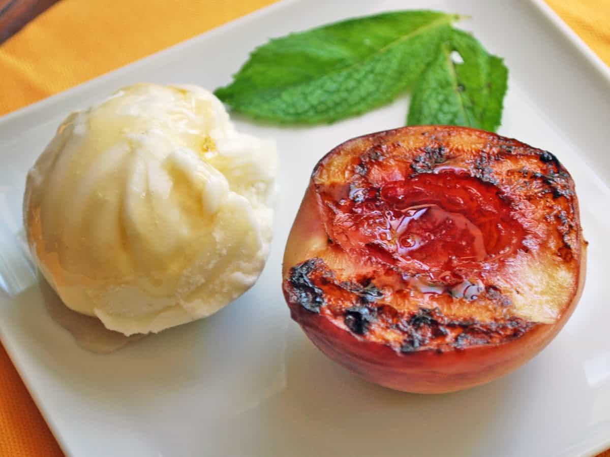 A grilled peach half is served with a scoop of frozen yogurt.