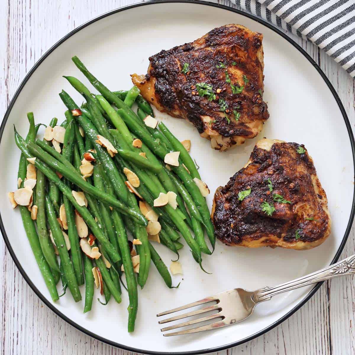 Green beans almondine are served as a side dish to jerk chicken.