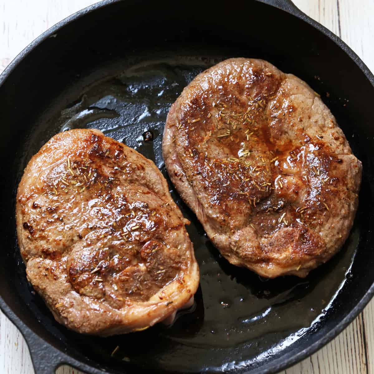 Two lamb steaks in a cast-iron skillet.