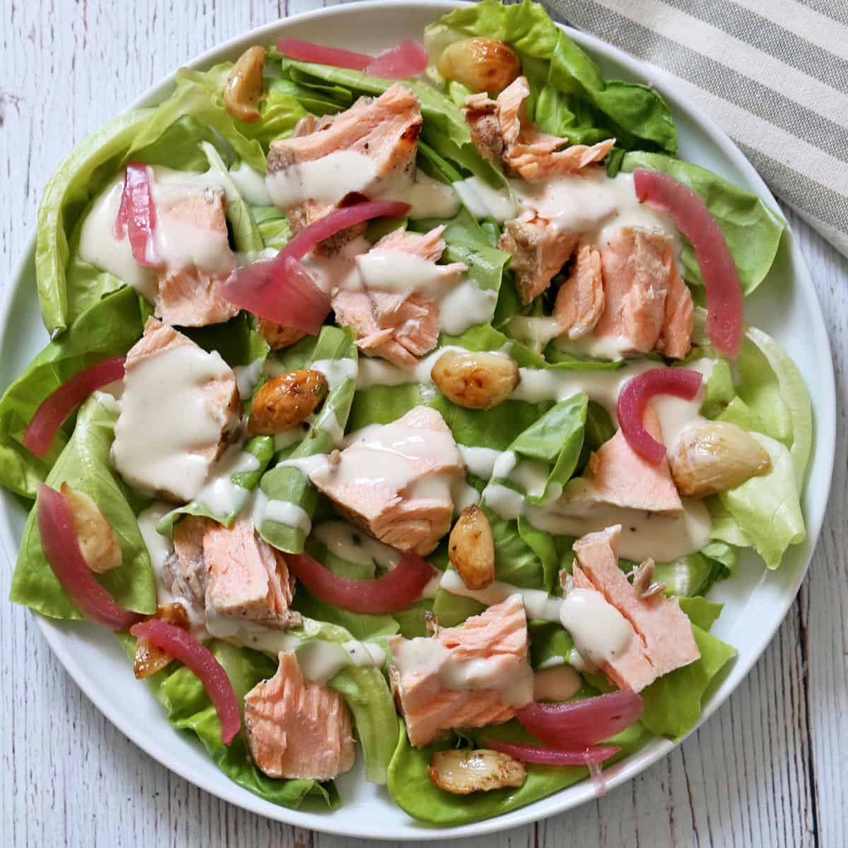 A plate with lettuce, leftover salmon, garlic cloves, and roasted red onions.