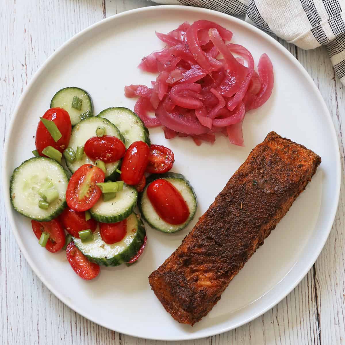 Pickled red onions are served with salmon and a salad.
