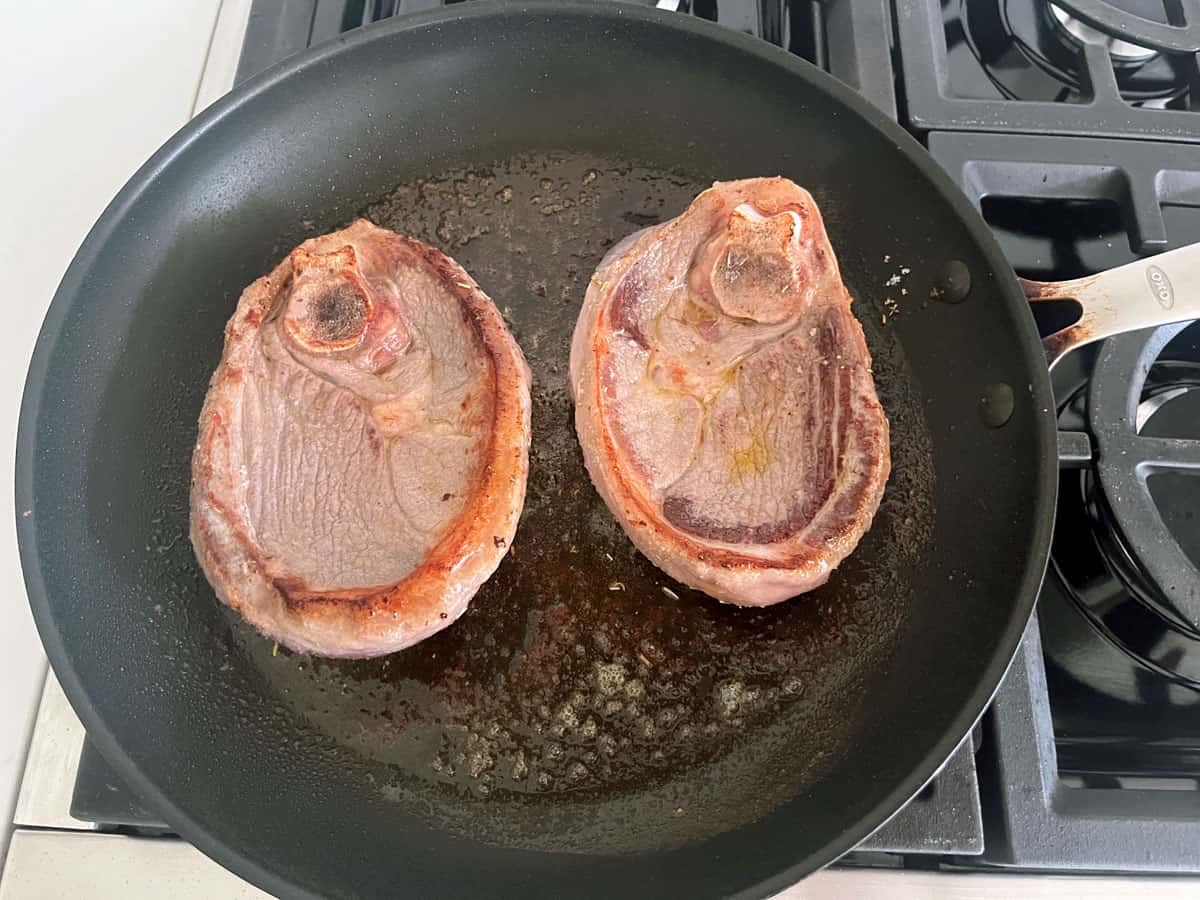 Two lamb steaks have curled in the skillet.
