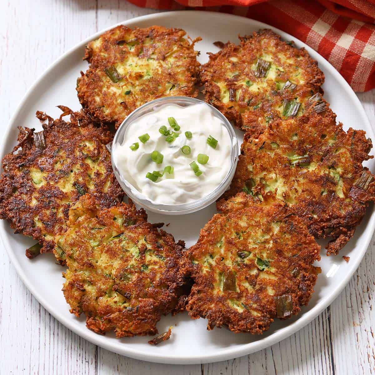 Zucchini fritters are served on a white plate with a sour cream dip.