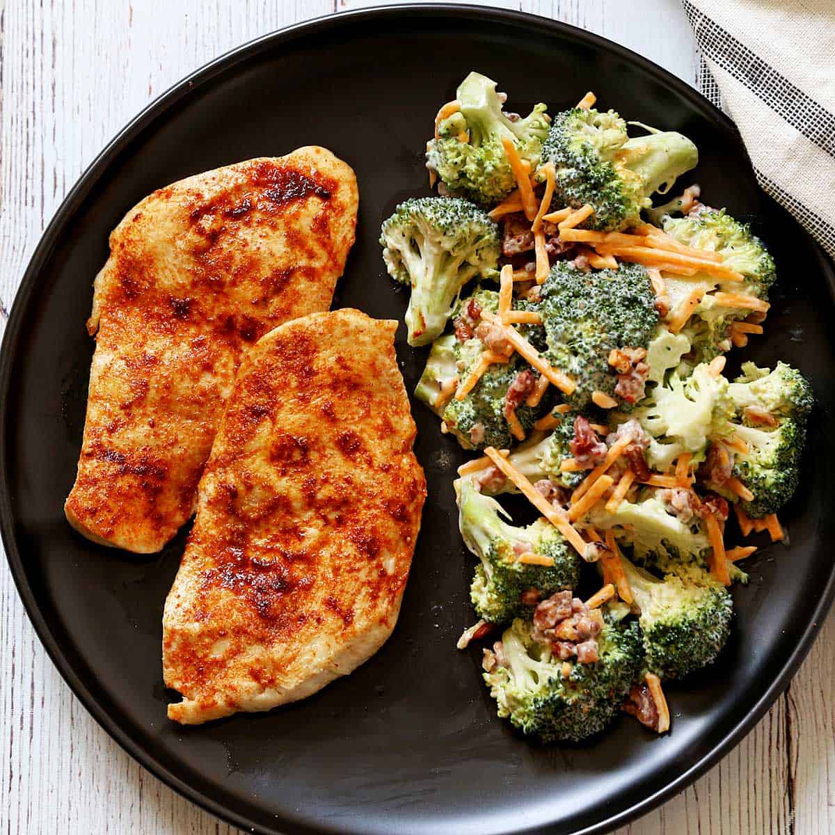 Two pieces of broiled chicken are served with broccoli salad.