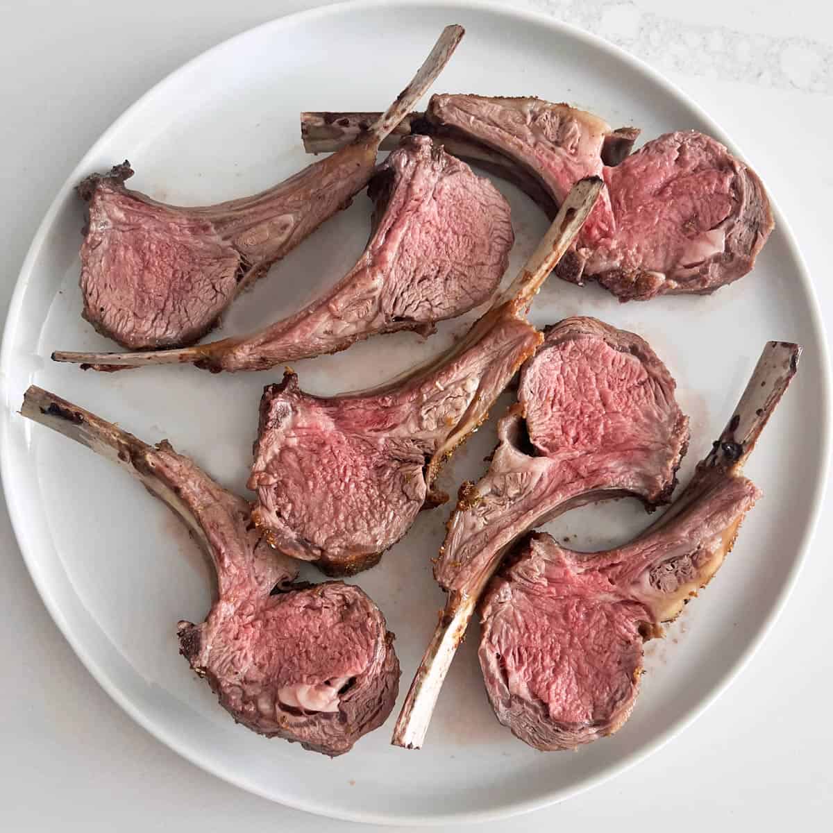 Ribs cut from a roasted rack of lamb are arranged on a white plate.