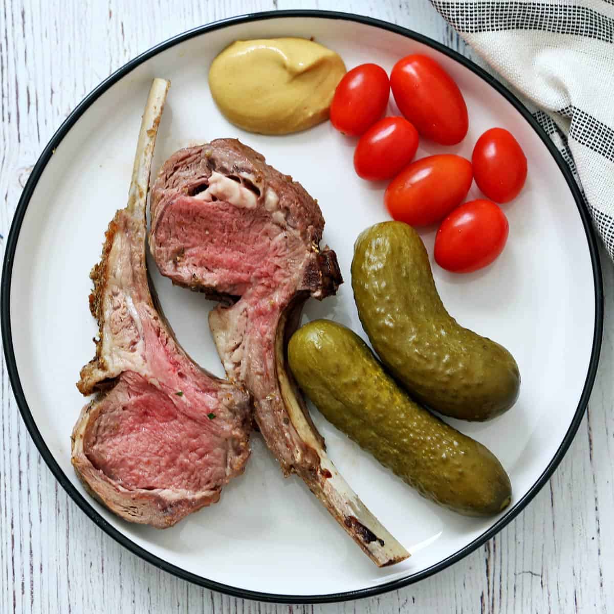 Rack of lamb leftovers are served with tomatoes, cucumber pickles, and mustard.