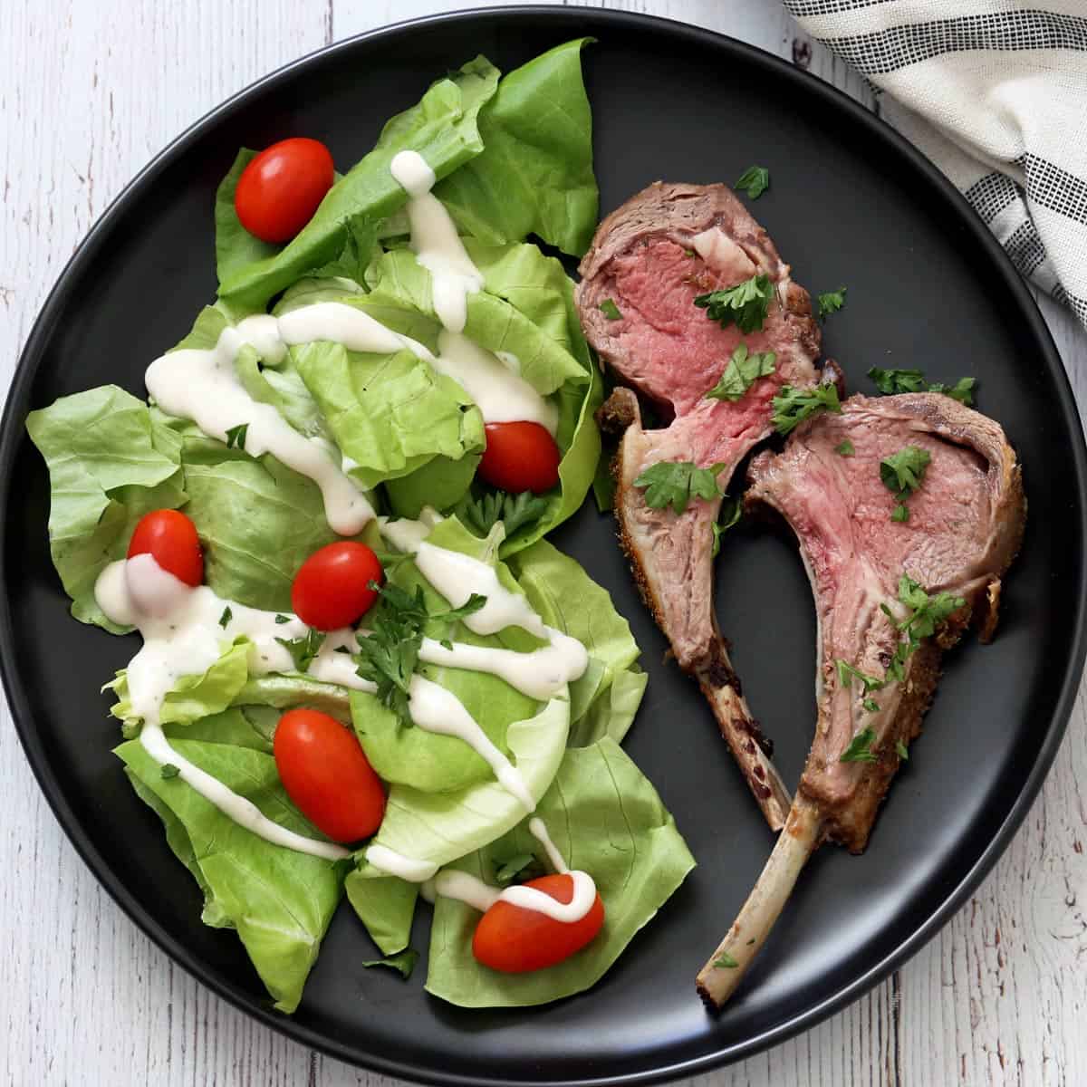 Two ribs that were cut from a roasted rack of lamb are served with a salad.