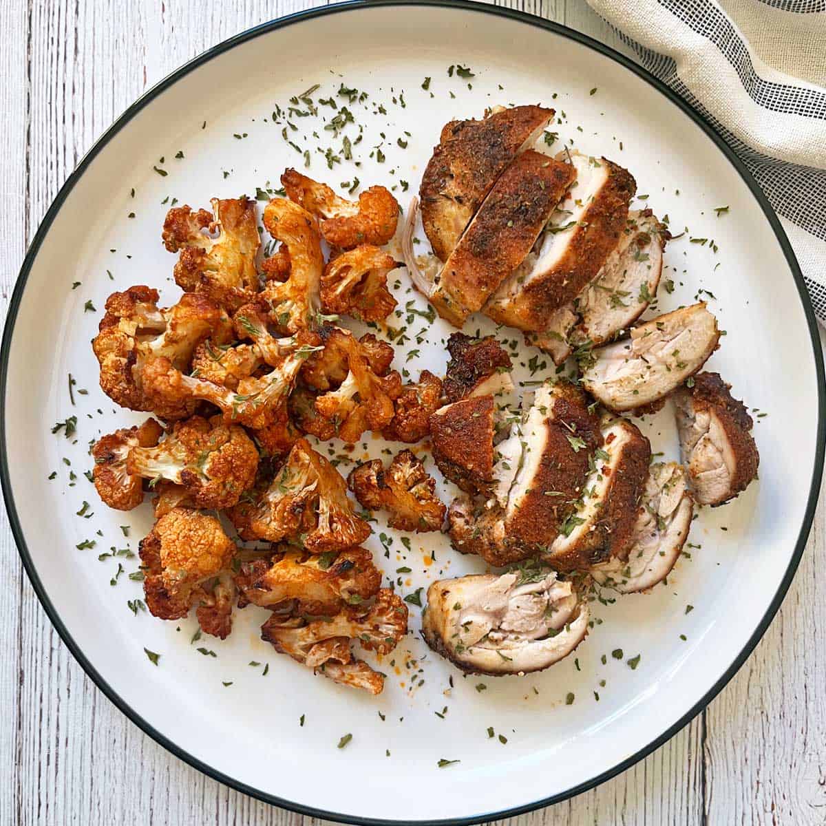 Reheated leftovers of Cajun chicken and buffalo cauliflower are served on a white plate.