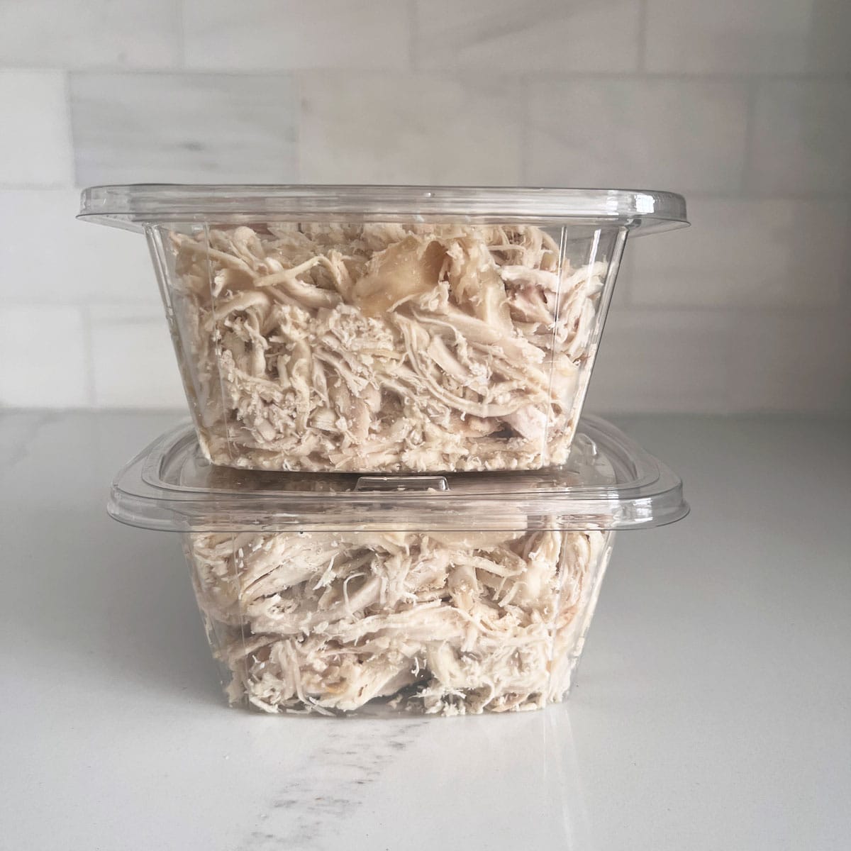 Two packages of shredded rotisserie chicken on a white counter.