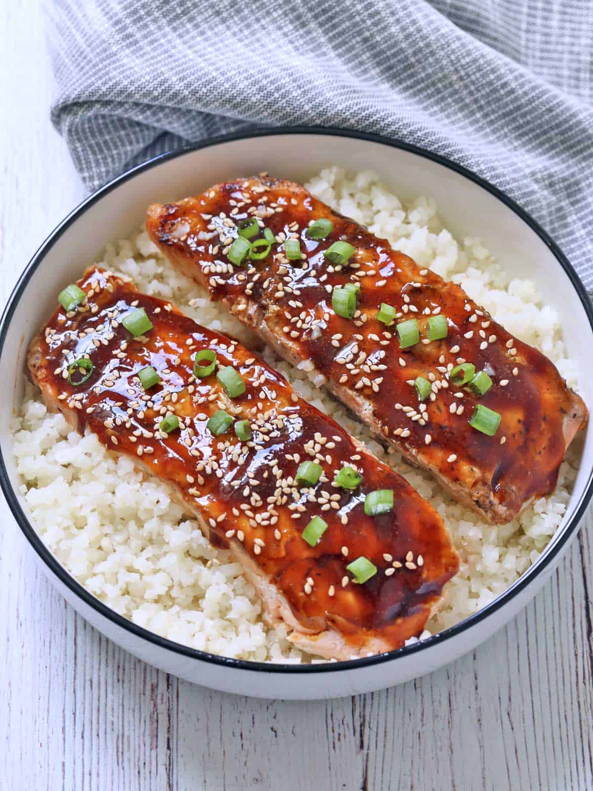 Teriyaki salmon is served in a bowl on a bed of cauliflower rice.