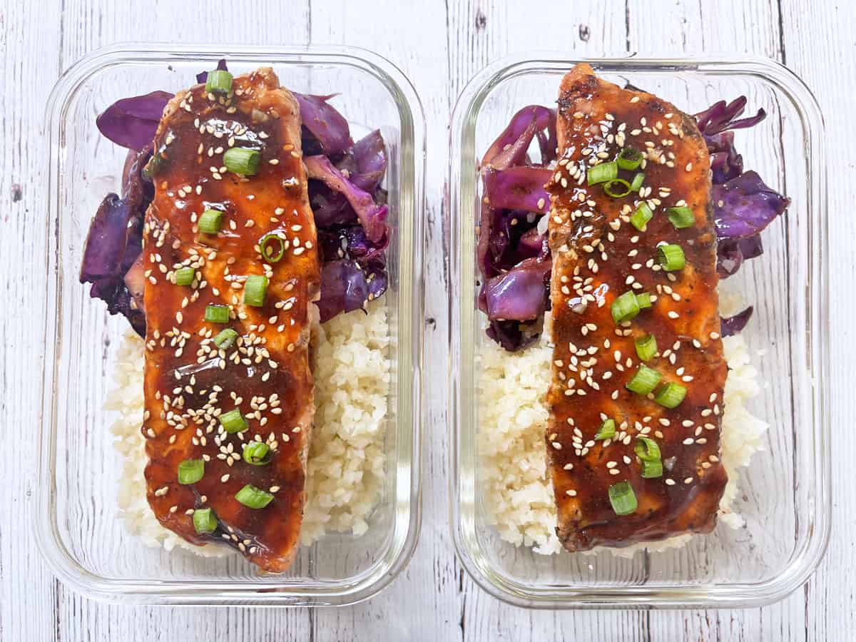 Meal prep containers with teriyaki salmon, cauliflower rice, and cabbage stir-fry.